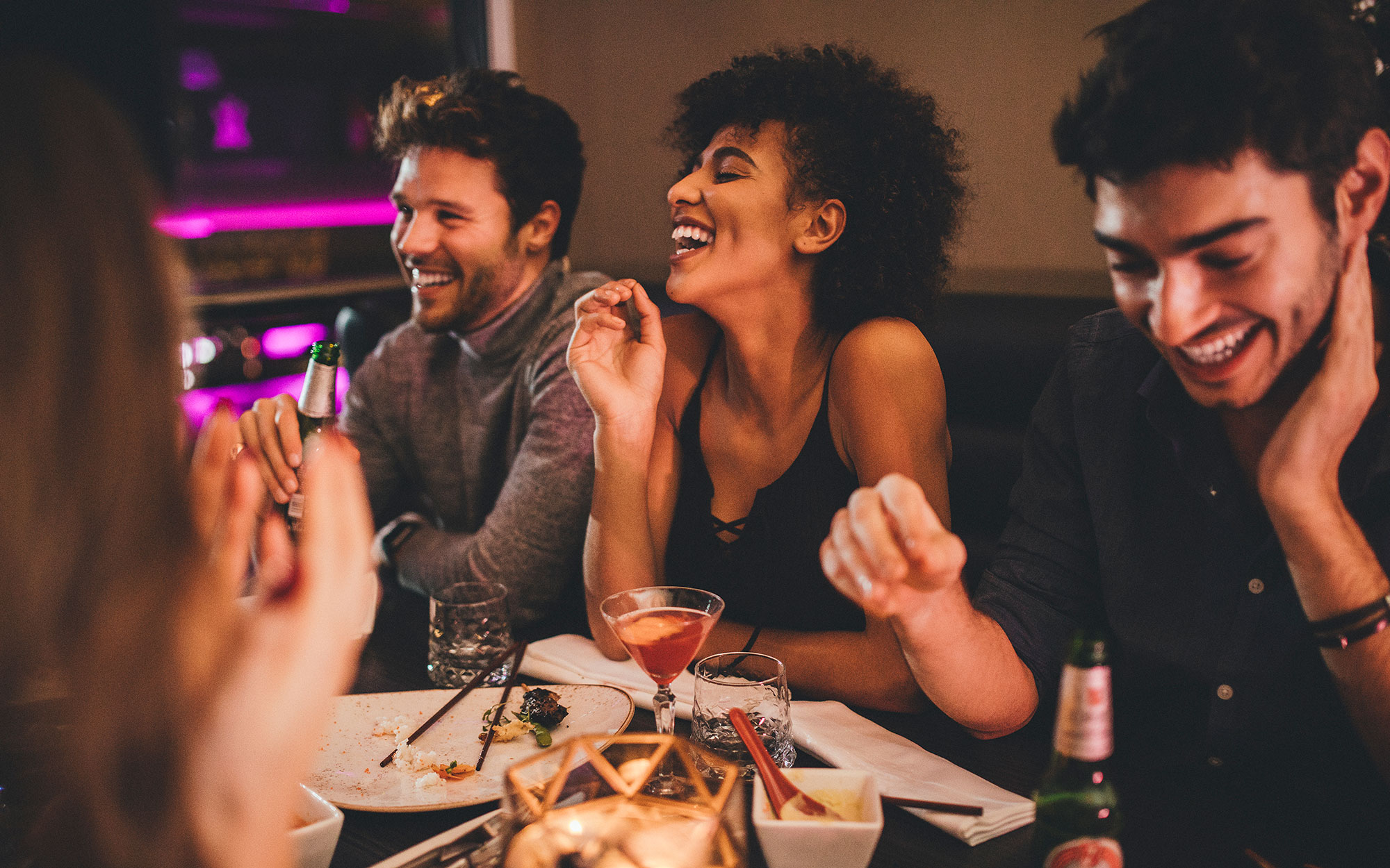 Ethnically diverse friends at a bar with cocktails laughing and having a good time in a nightclub