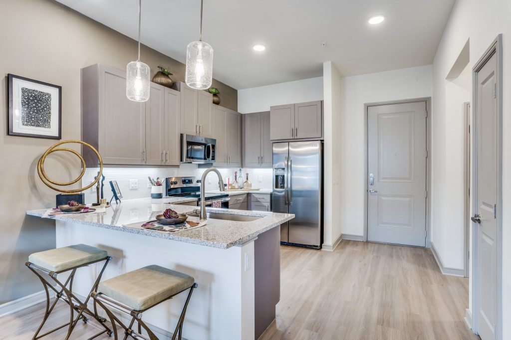L shaped kitchen with bar top seating, stainless steel appliances, large single basin sink, pendant lighting, and upper and lower cabinets
