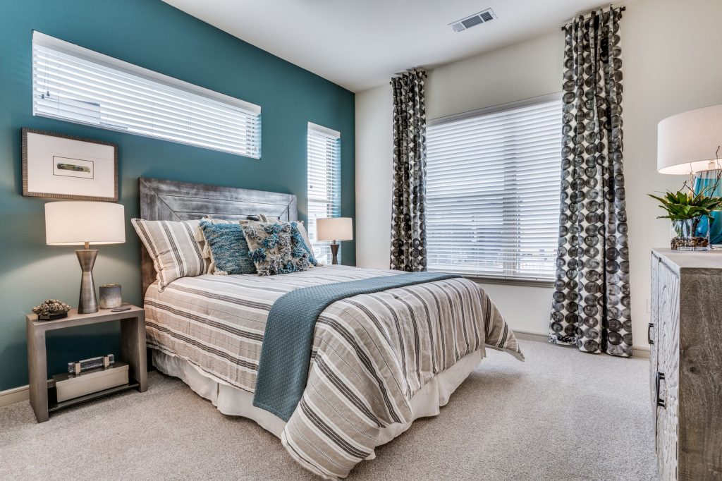 Bedroom with carpet and teal accent wall, a full size bed, large window with patterned drapes and dual side tables with lamps