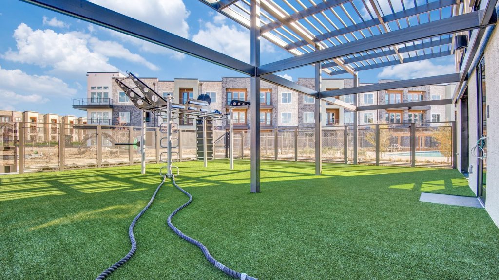 Outdoor Crossfit area with battle ropes, turf ground, workout jungle gym and apartments in the background