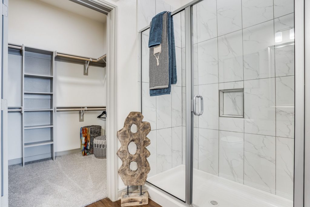 Walk-in shower with tile backsplash, abstract decorative sculpture, and walk in closet with shelving